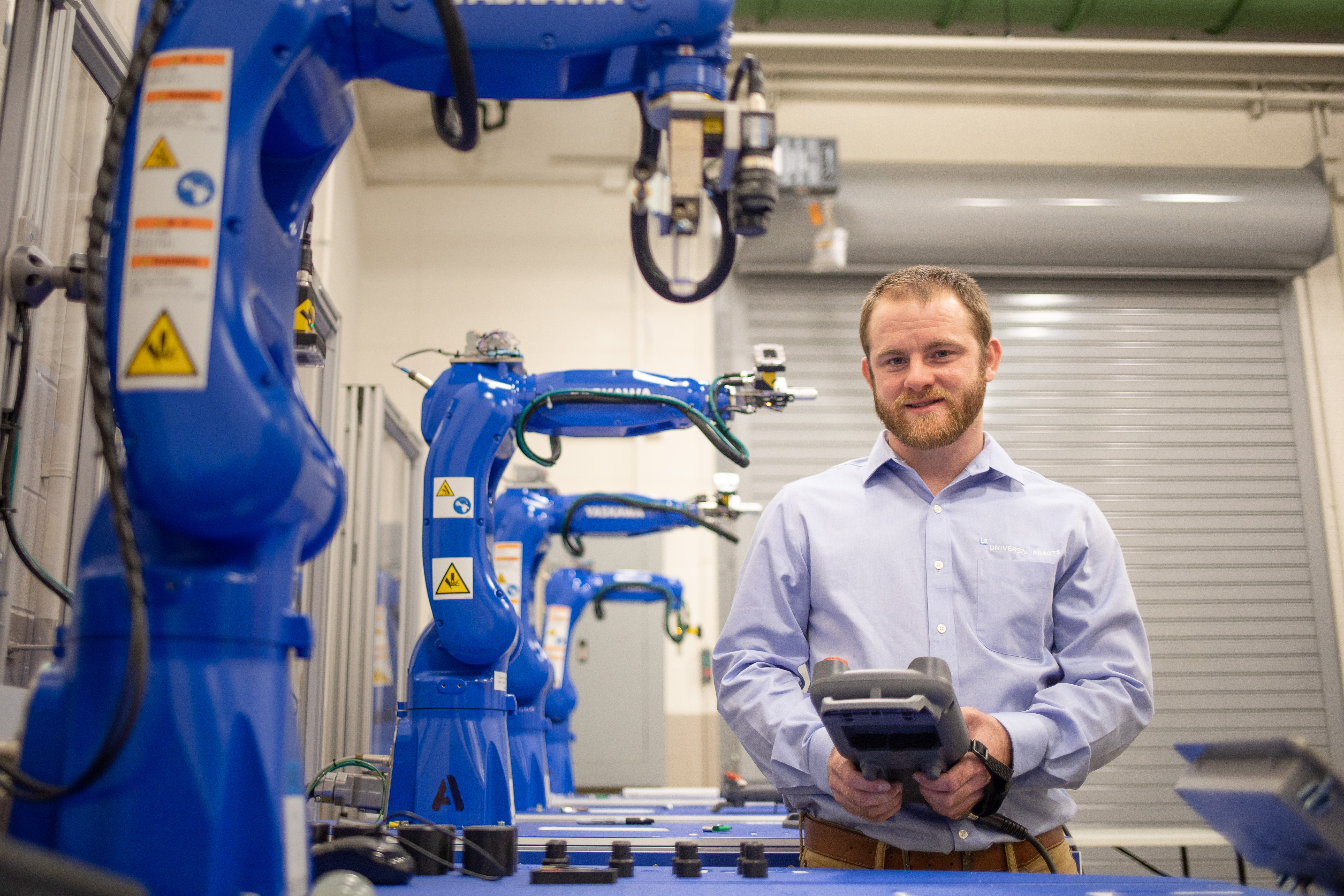 LeGrand Sommers standing behind a robotic arm and holding a PLC controller at Motlow’s ARTC in McMinnville.